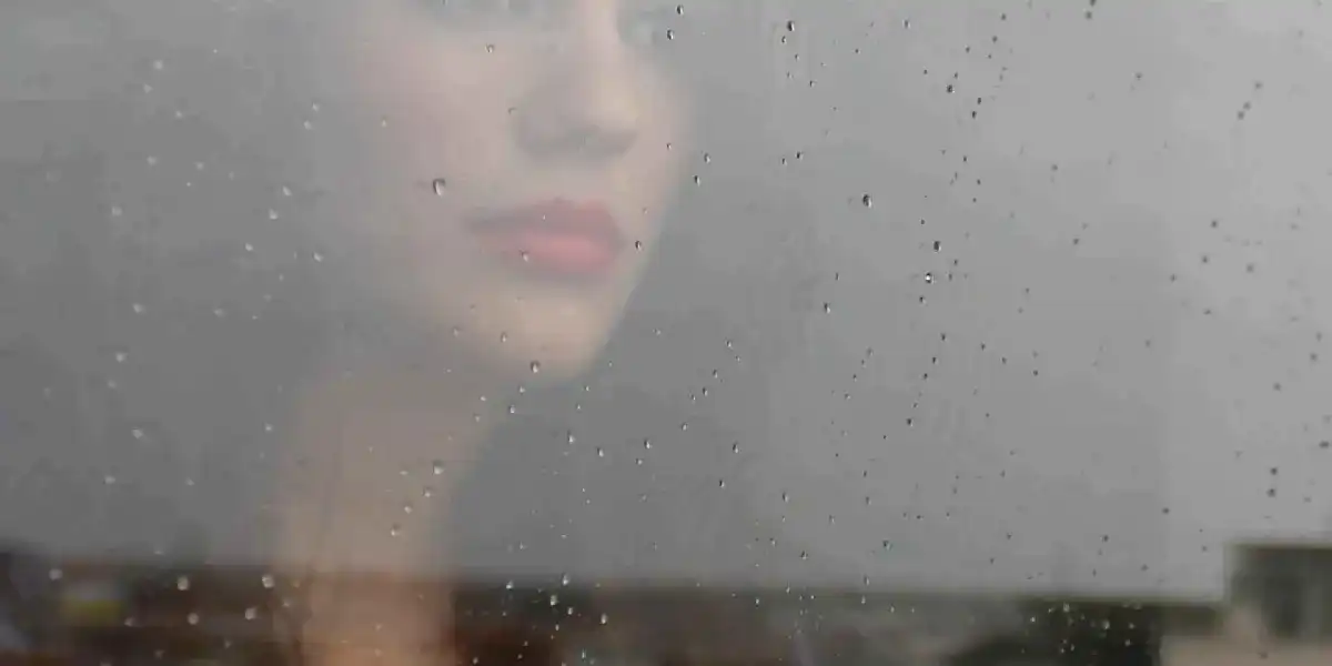 Pensive woman looking out a window at the rain